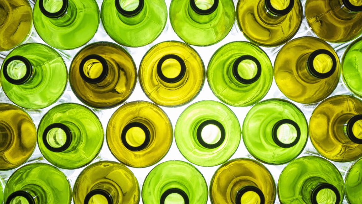 Draufsicht auf dicht aneinandergereihte grüne und gelbe Glasflaschen, von unten beleuchtet.