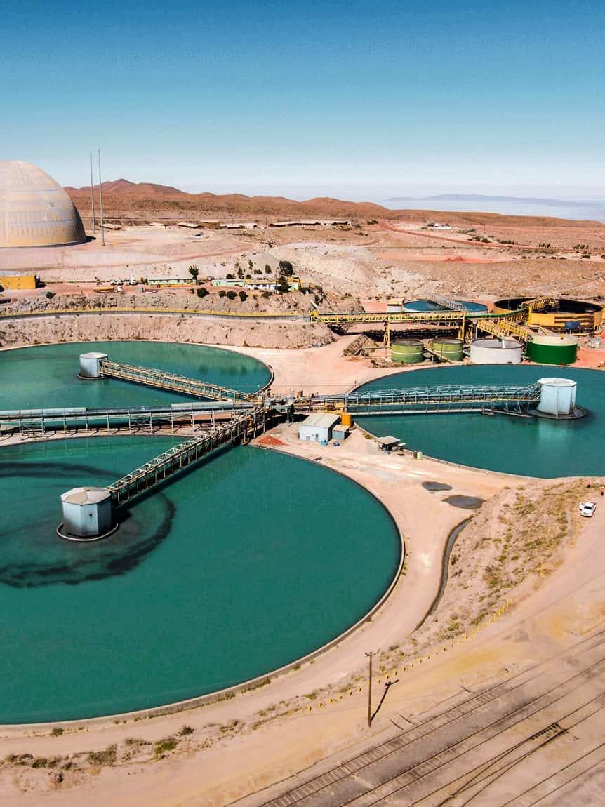 Luftaufnahme einer industriellen Bergbauanlage mit mehreren großen, türkisfarbenen Absetzbecken in einer trockenen Wüstenlandschaft.
