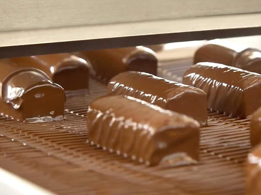 Nahaufnahme von handgemachten Schokoladenpralinen mit dekorativen weißen Mustern auf einer Bambusmatte.