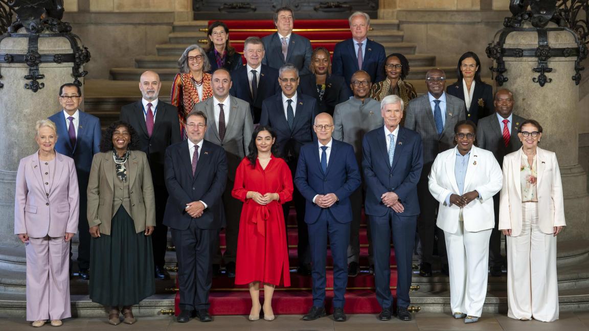 Gruppenfoto von vielen Personen in formeller Kleidung auf einer Treppe in einem repräsentativen Innenraum.