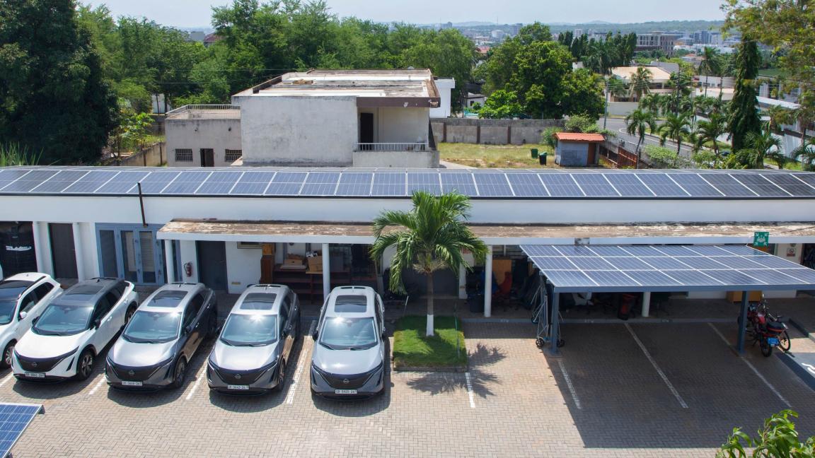 Solar panels on the roof of a building next to a car park with parked cars.