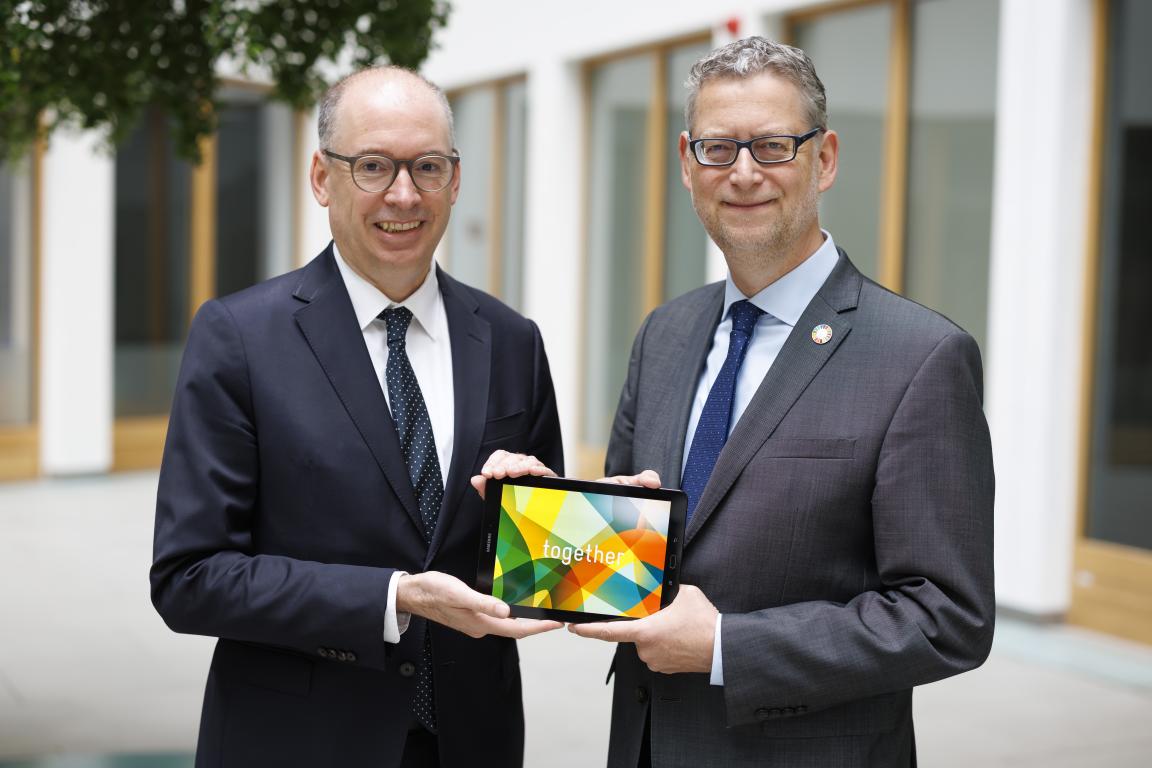 Two men in suits and ties are holding a tablet together, displaying colourful graphics and the word ‘Together’