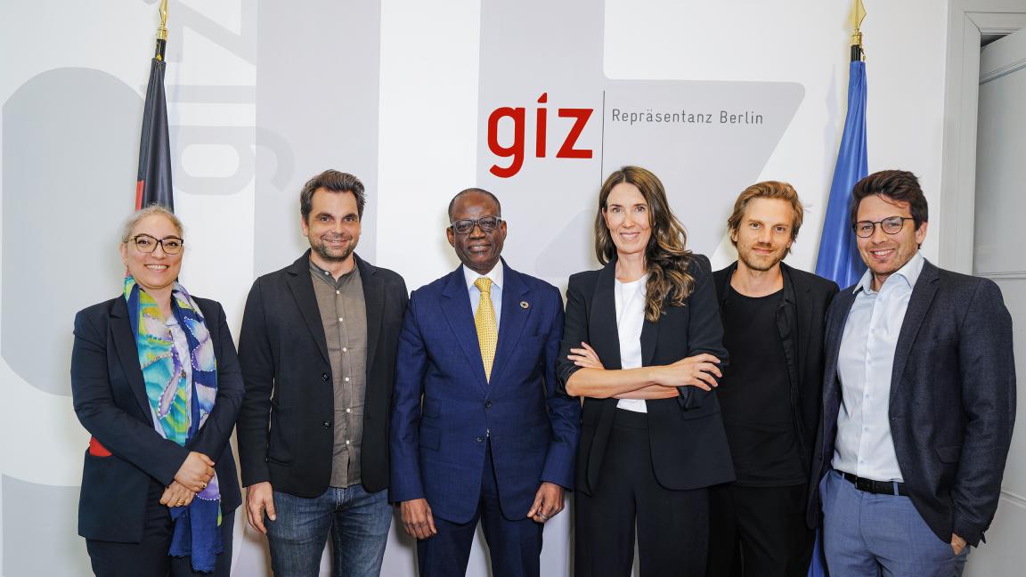 Sechs Personen in Anzügen posieren vor einer Wand mit „giz“-Logo
