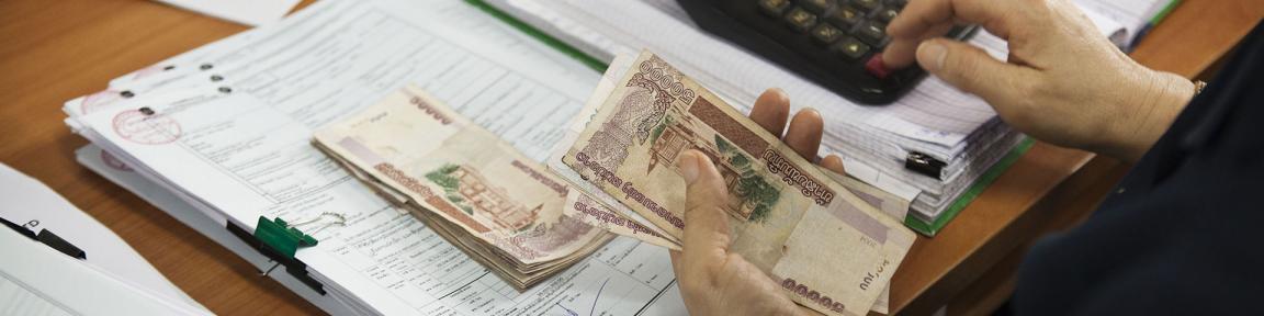 Eine Person hält Geld in der Hand und tippt auf einem Taschenrechner