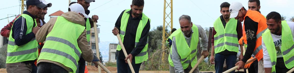 Eine Gruppe männlicher Cash Worker schaufelt Kies, um eine Straße zu reparieren. Copyright: Eliana-Keshawty
