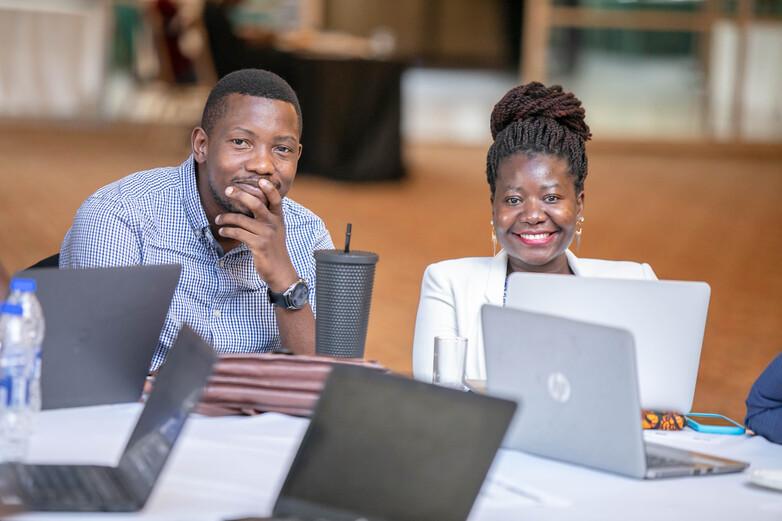 A woman and a man sit at a table with laptops in front of them.