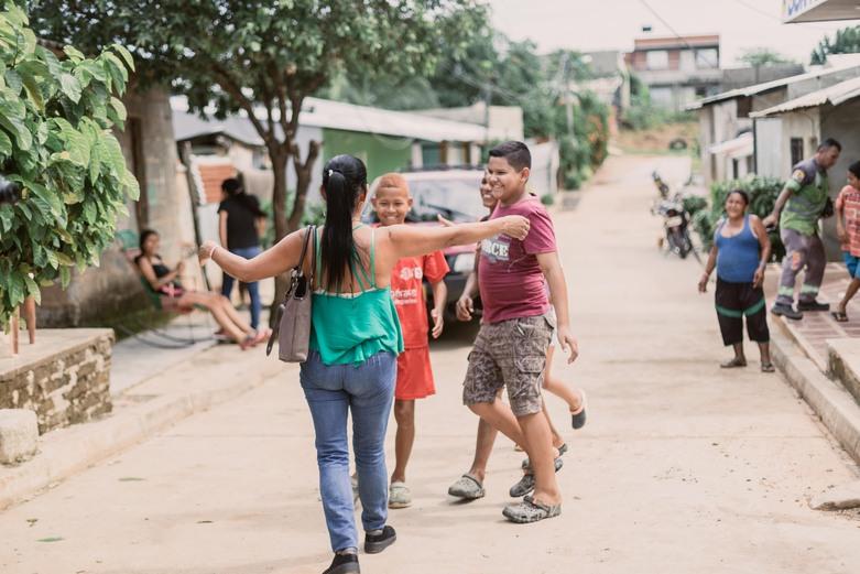 On a street, a woman walks towards three young people with her arms open.