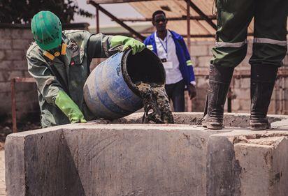 A sanitation worker in personal protective equipment empties a barrel of collected faecal sludge.