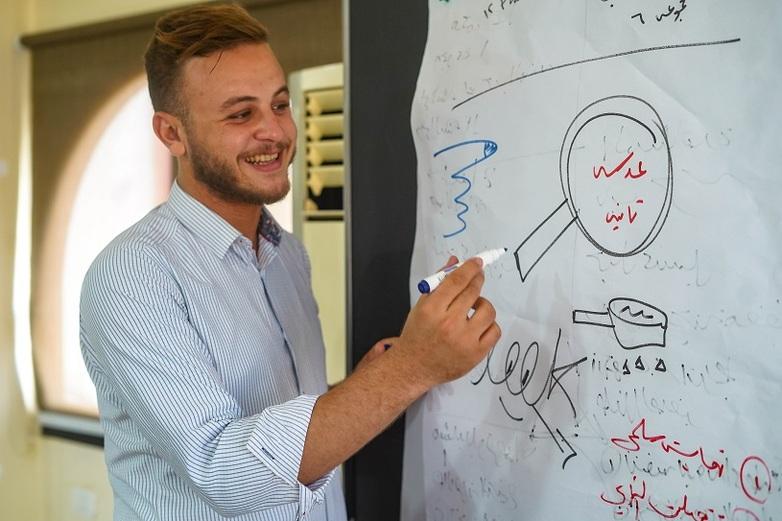 A man draws on a workshop poster, smiling.