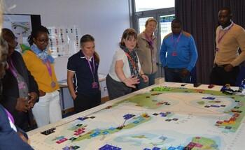 People stand round a large planning map on a table as part of a marine spatial planning simulation game. © GIZ MARISMA / Linda Kasheeta