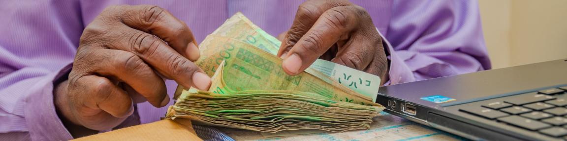 Deux mains comptant une liasse de billets de banque.