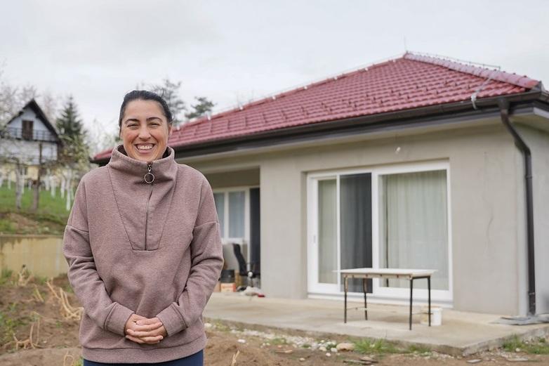A smiling woman stands in front of her house in Bosnia and Herzegovina after energy efficiency measures have been carried out on the building.