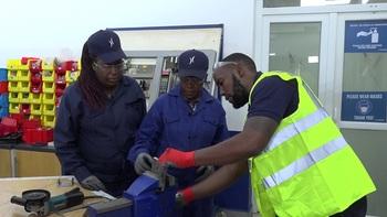 A trainer at Krones EA (with reflector jacket) shows two trainers from Kiambu Institute of Science and Technology (KIST) how to position a metal object before a grinding process. This exercise was part of training trainers ahead of the first intake of Industrial Mechatronics students. GIZ/AnchorBay