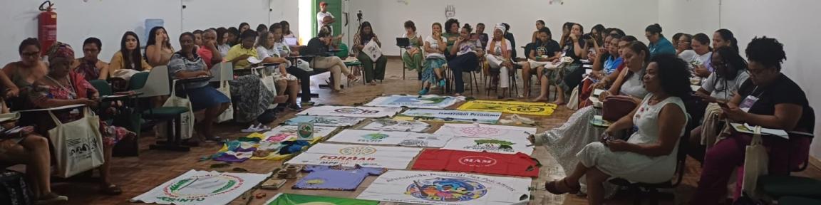 Die Teilnehmerinnen des Workshops „Girls and Women Protagonism in Climate Justice“ (Mädchen und Frauen für Klimagerechtigkeit) in Brasilien sitzen in einem Raum, auf dessen Boden Plakate unterschiedlicher Organisationen ausgebreitet sind.