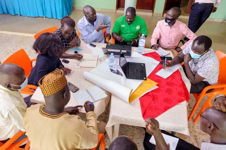 A group of people with notebooks discuss a topic at a working table.