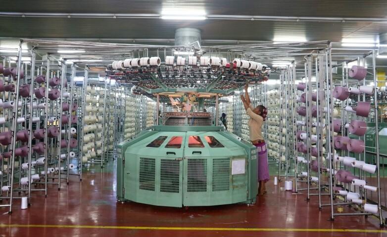 A female worker adjusting a large circular knitting machine in a textile production facility.