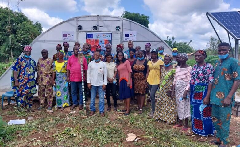 A group of farmers and trainers standing in front of a greenhouse and solar panel, showcasing agricultural innovations in Nigeria that includes business modelling development.