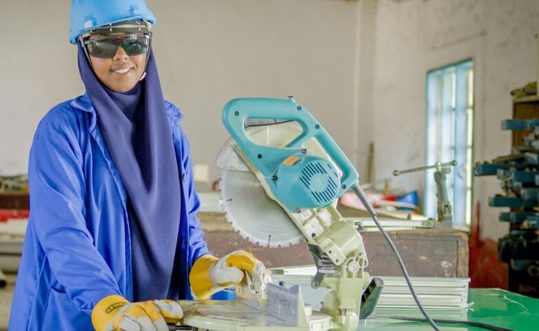 A trainee wearing safety gear operating a circular saw as part of an interior design and carpentry training in Somalia.