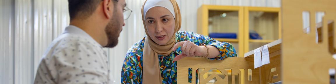 Eine Vorgesetzte schult einen Mitarbeiter, der an einem Computer sitzt.