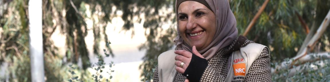 Eine Frau, die eine Weste mit Aufdruck „giz“ und „NRC“ trägt, steht in einem Wald.