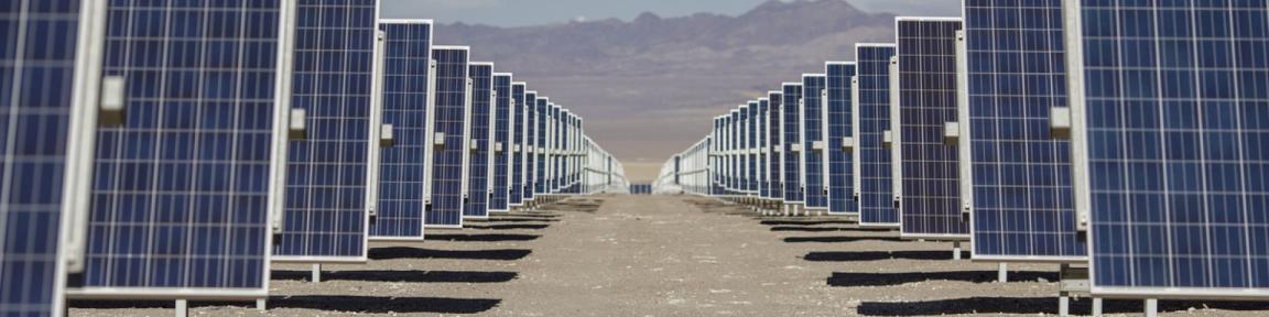 Rows of solar panels installed in a desert landscape with mountains in the background, illustrating renewable energy development in Mexico.