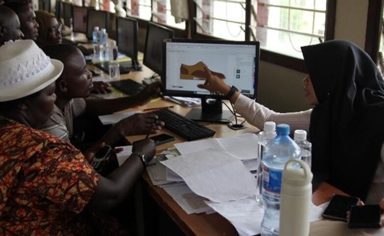 A trainer guiding participants in designing footwear on a computer as part of technical training in leather production.