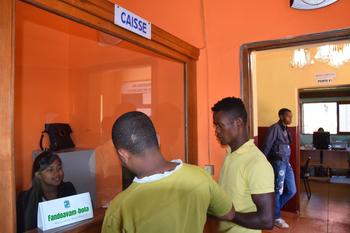 Deux hommes se tiennent devant le guichet d’une administration et parlent avec une employée.