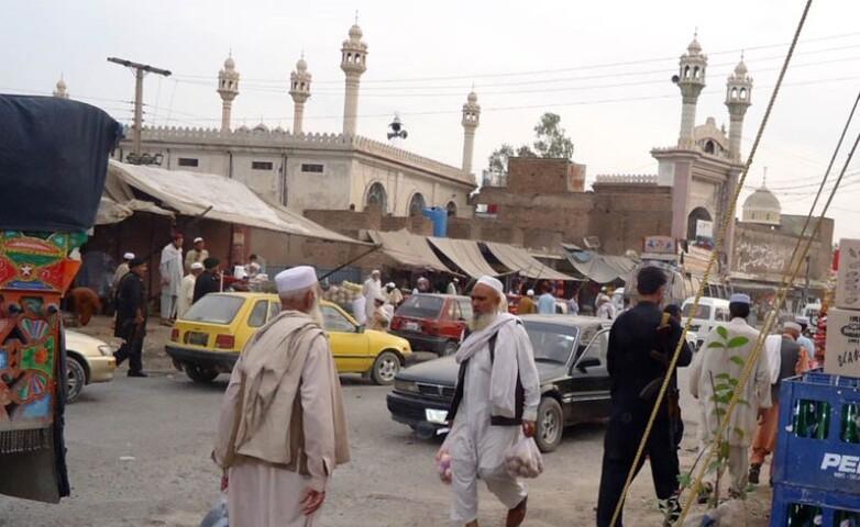 Men walking in a small-town market in front of a mosque.