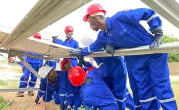 Trainees in blue uniforms and red helmets installing solar panels during a renewable energy training session in Somalia.