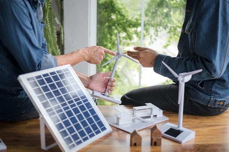 Modelle einer Windmühle und Solaranlage stehen im Vordergrund. Im Hintergrund zeigen Personen auf das Modell einer Windkraftanlagen.