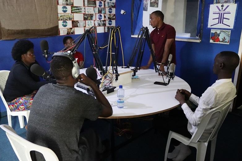 Fünf Personen an einem runden Tisch, eine von ihnen stehend. Vor ihnen sind Mikrofone und Mischpulte aufgebaut. Copyright: GIZ