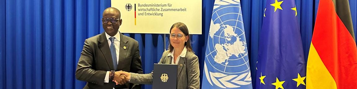 Lacina Koné, CEO von Smart Africa, und BMZ-Abteilungsleiterin Birgit Pickel geben sich vor den Flaggen der UN, der EU und Deutschland die Hand.