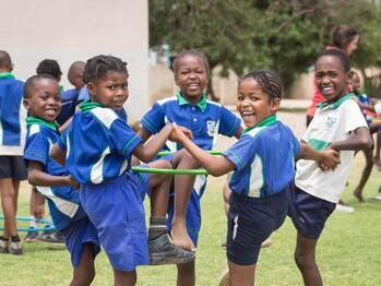 In a game, children hold hands and carry a tyre on their legs.