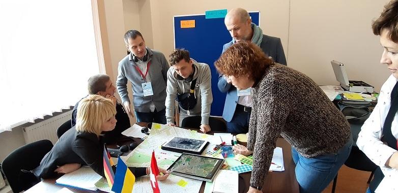 Sieben Personen sitzen und stehen um einen Tisch mit Plänen und Karten herum und besprechen sich. Copyright: GIZ