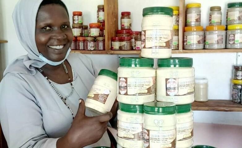 A woman displaying jars of shea butter products in her shop in Arua, Uganda, after receiving business coaching and mentorship support from the project.