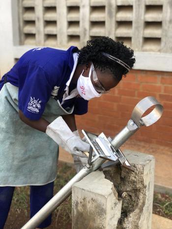 A mechanic wearing protective equipment works on a metal hand-pump component.