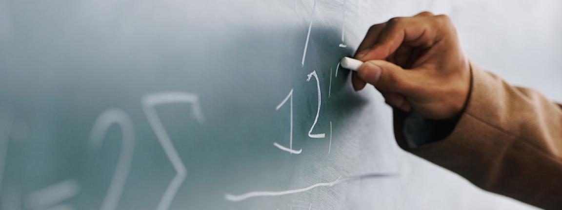 Eine Person schreibt mit Kreide Zahlen an eine Tafel.