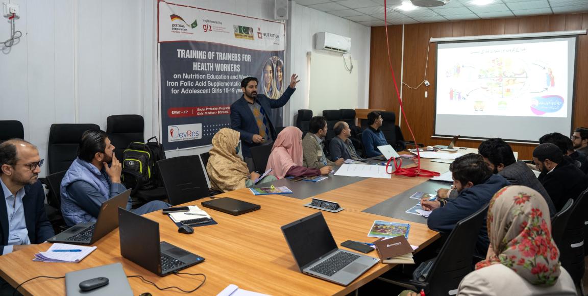 Several people are sitting at a table, working on laptops and exchanging ideas.
