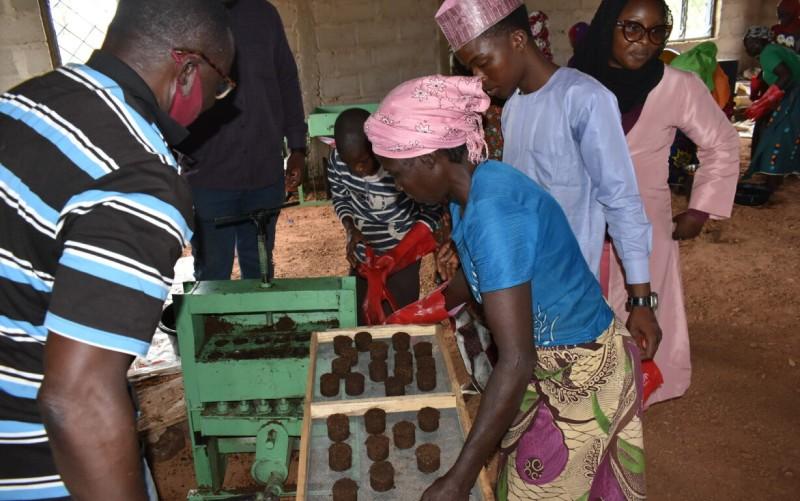 Mehrere Personen stellen im Rahmen eines Workshops Brennstoffbriketts mit einer handbetriebenen Maschine her.