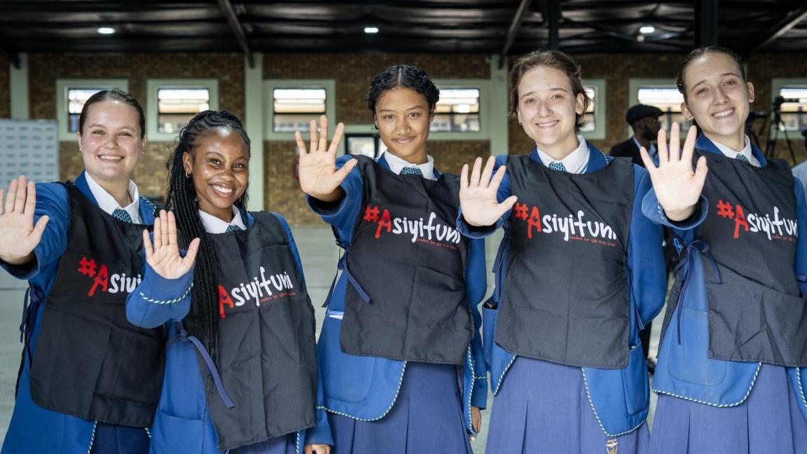 Fünf Mädchen in Schuluniform und Weste einer GBV-Initiative halten ihre Hände als Stopp-Signal nach vorne.