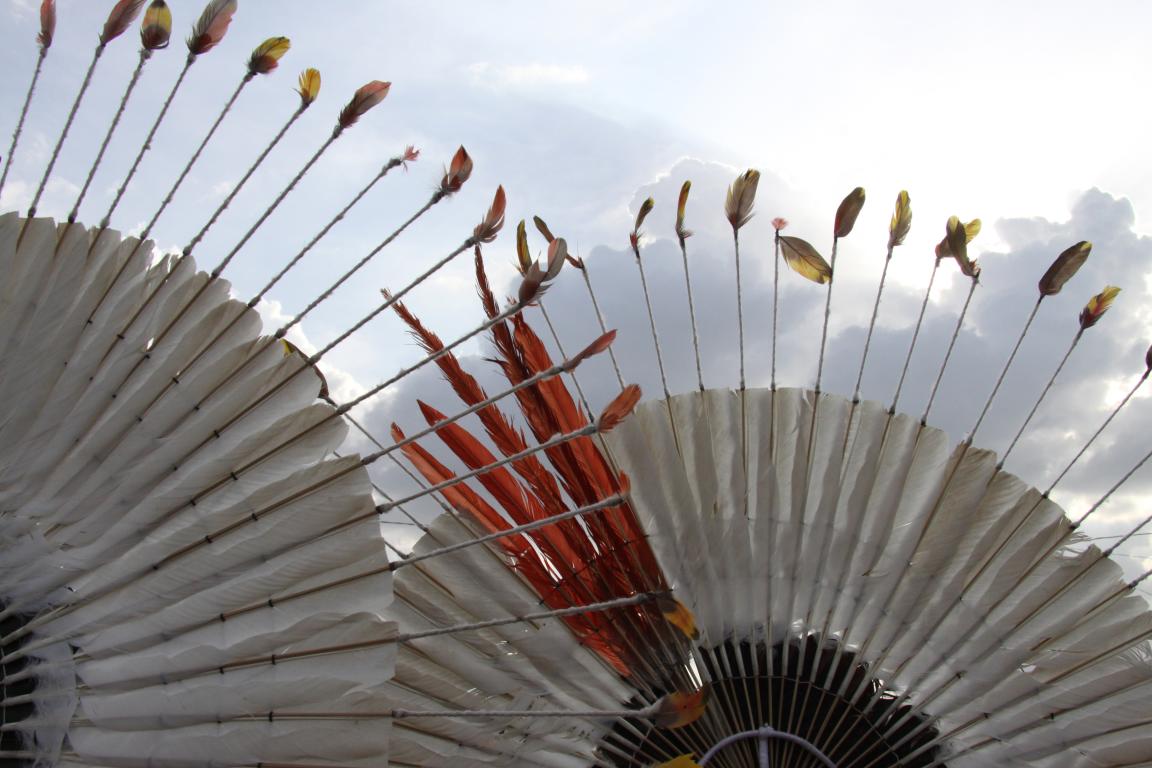 Close-up view of indigenous feather headdresses with colourful feathers against a cloudy sky background.