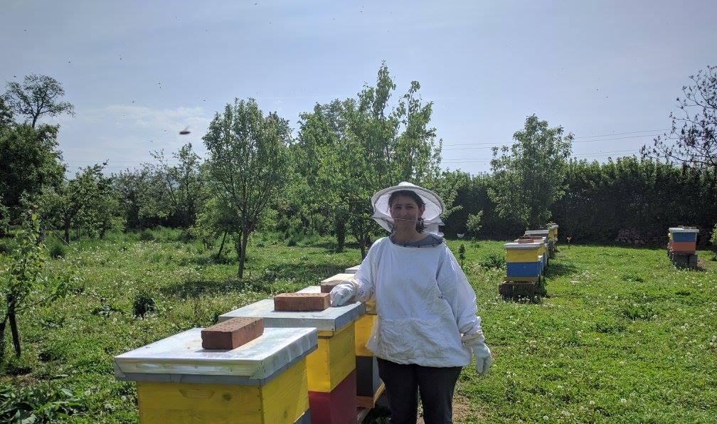A woman in protective clothing next to beehives.