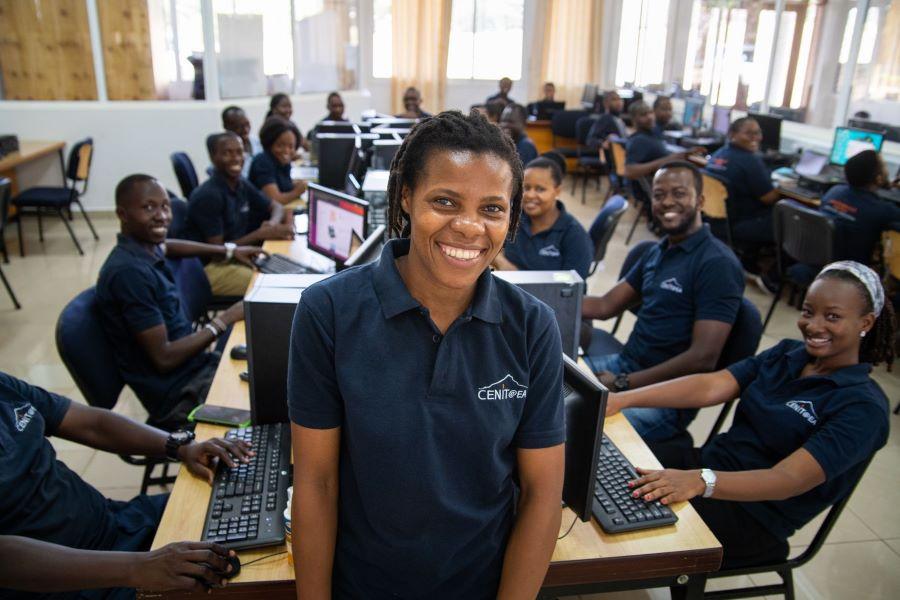 Eine Schulklasse sitzt an Computern, eine Schülerin im Vordergrund lächelt in die Kamera.