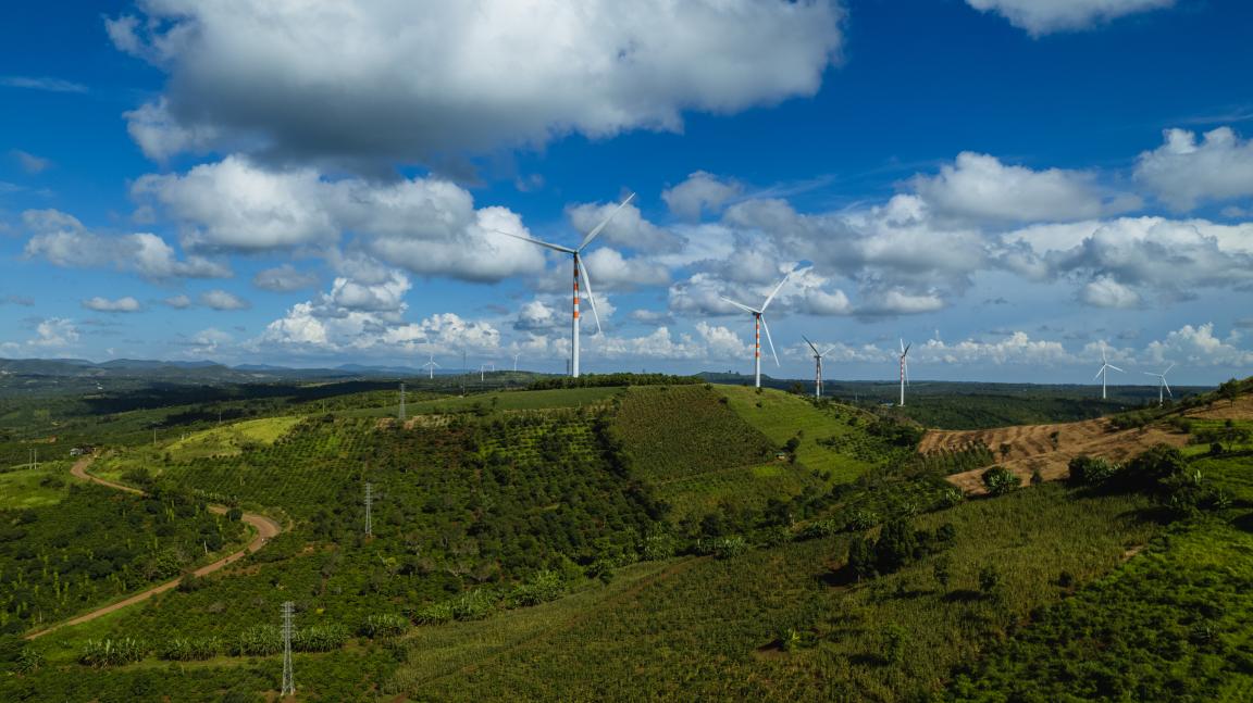 Windräder stehen in einer grünen, hügeligen Landschaft in Vietnam.