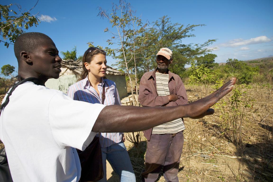 Several people are standing in a field, and a man is pointing at something.