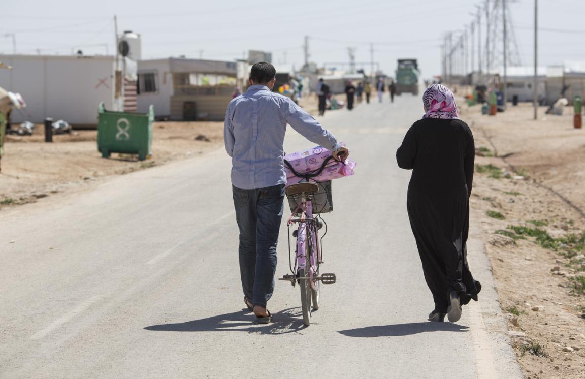 Two people pushing a bicycle on a road.