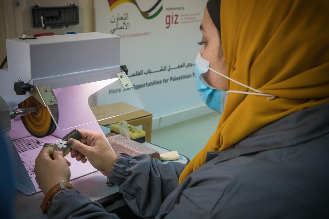 A woman wearing a hijab works on a machine in an industrial setting.