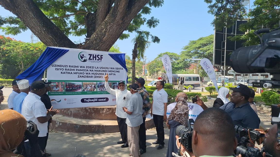 Several people standing in front of a Zanzibar Health Services Fund information board.