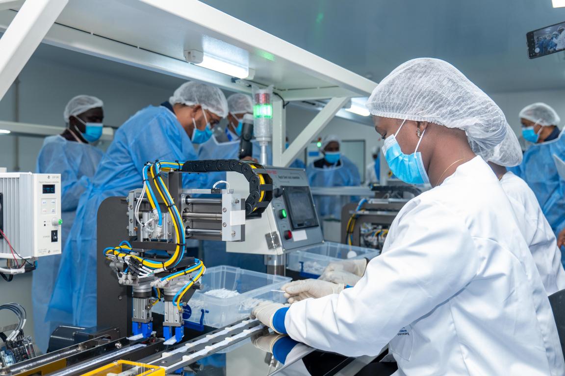 Une technicienne travaille dans une installation de production de tests de diagnostic rapide. D’autres collègues se trouvent à l’arrière-plan.