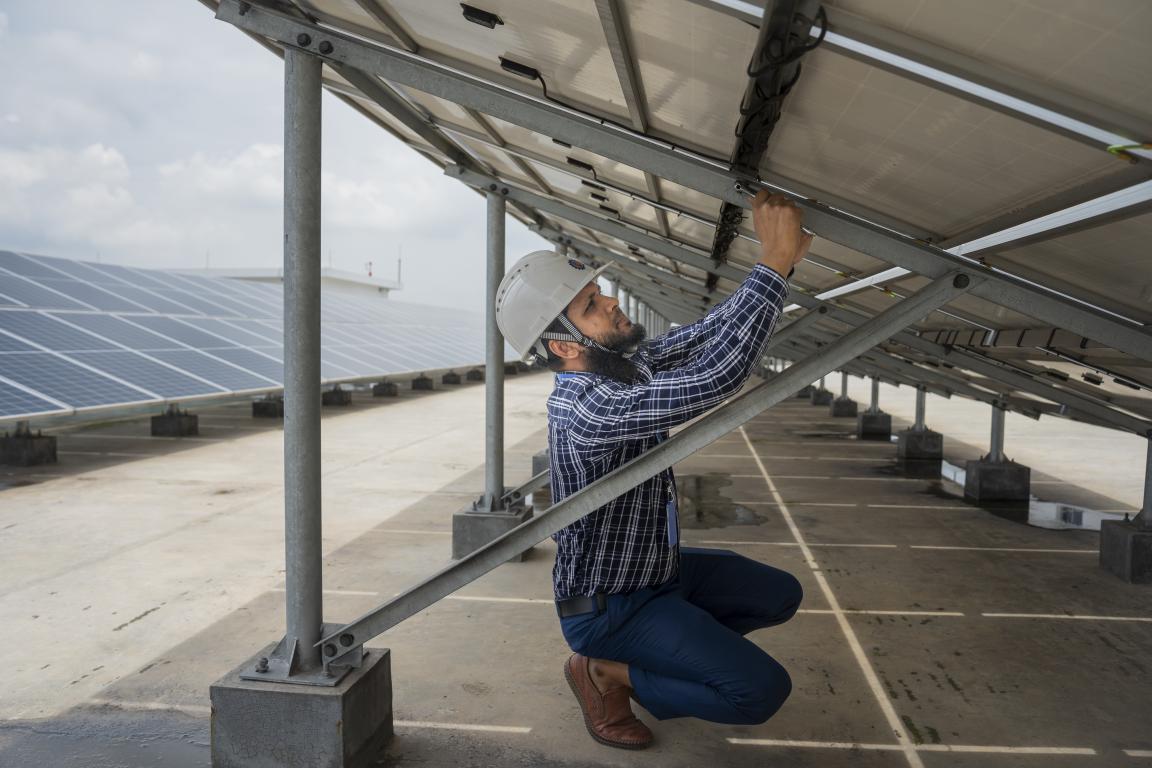A man in a safety helmet works on a solar panel in a solar park.
